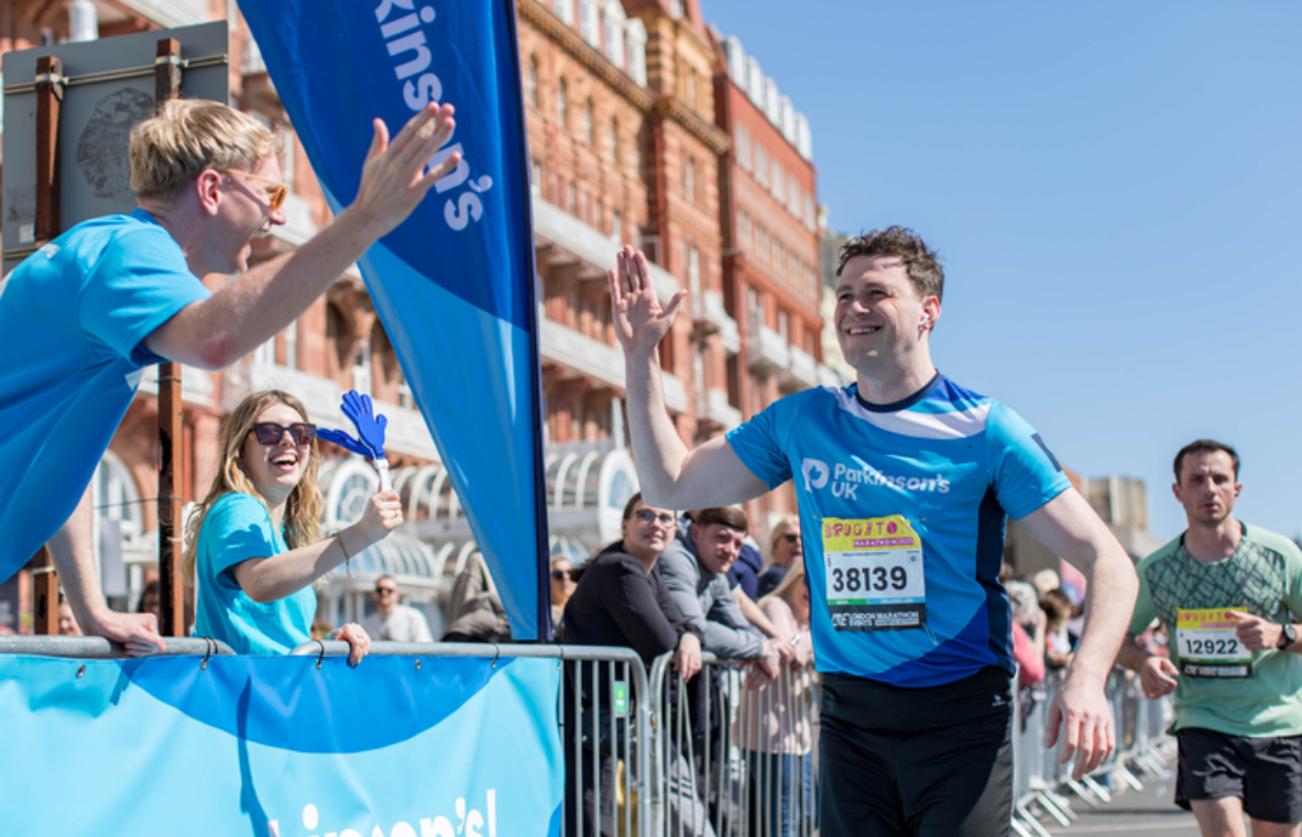A parkinson's UK running waving at a Parkinson's UK cheerpoint