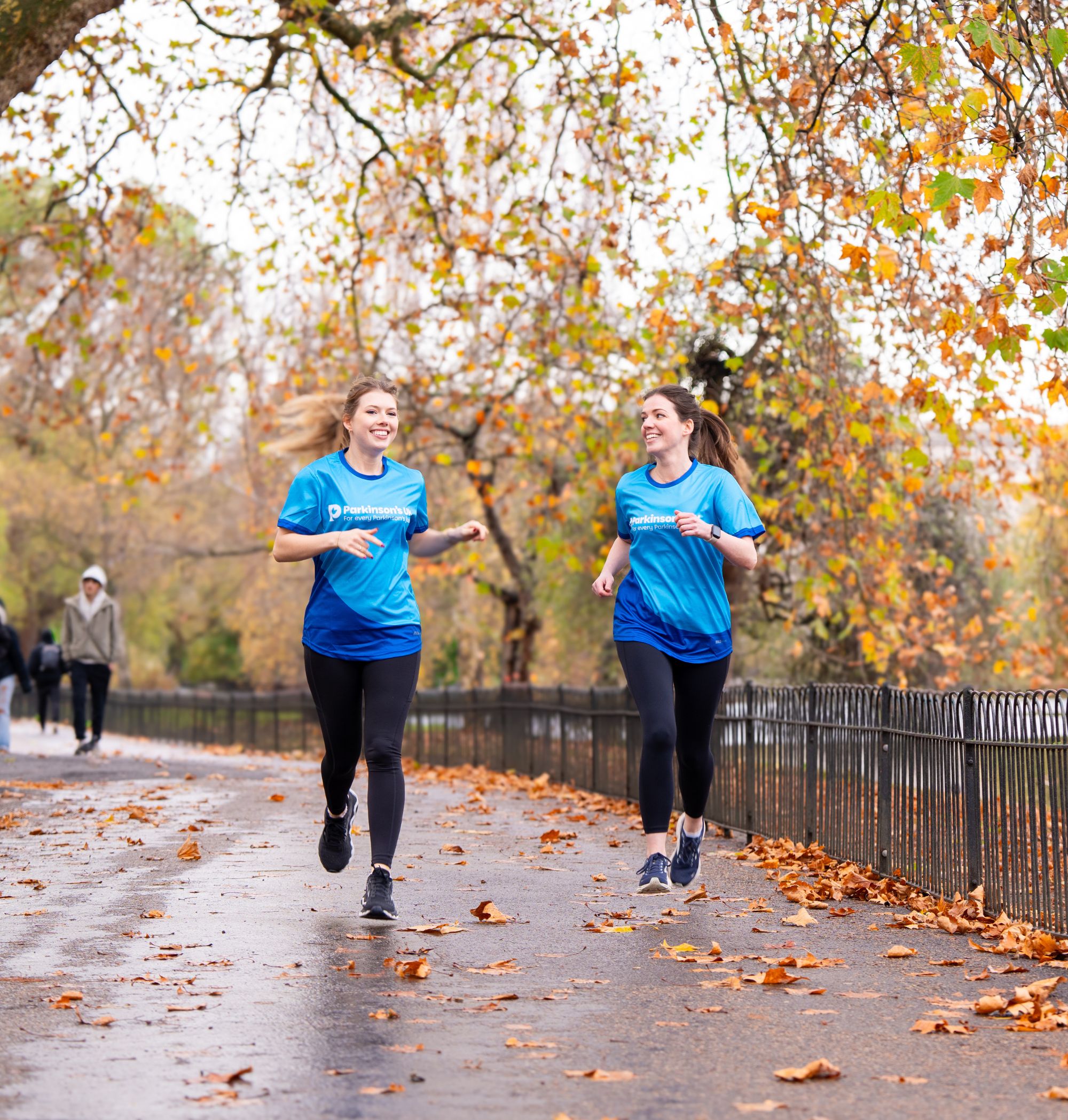Two women jogging through a park together.