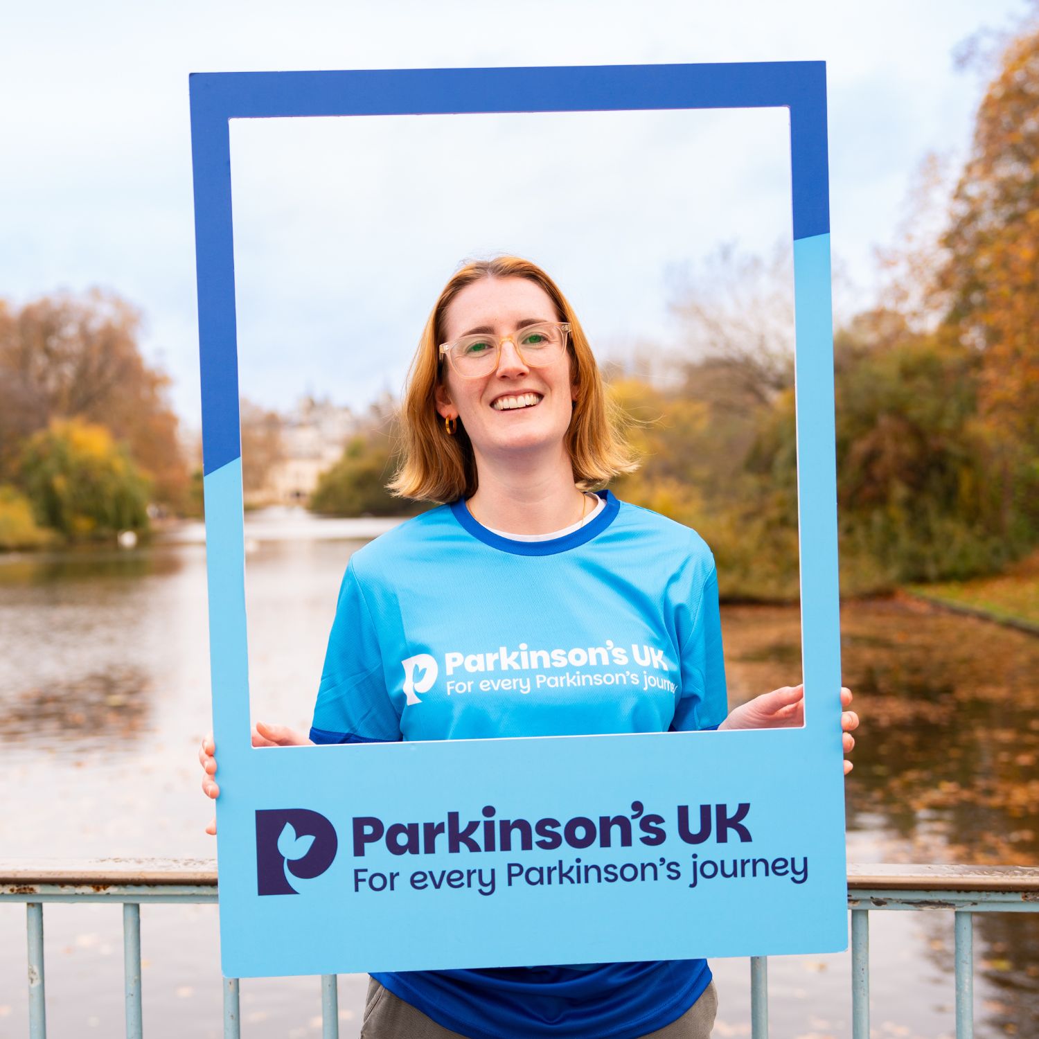 A woman poses holding a Parkinson's UK frame.